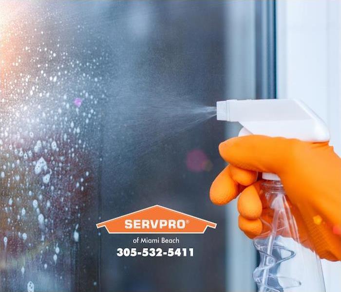 A orange-gloved hand is shown spraying a cleaning solution onto a glass door.